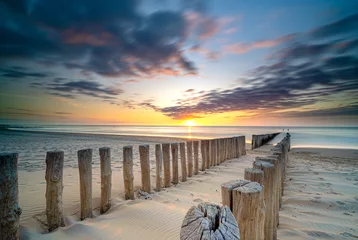 Foto op Aluminium Pole heads of wave-breakers close-up verdwijnen in de Noordzee in Nederland met zonsondergang op de achtergrond van de zee en bewolkte hemel © fotografiecor
