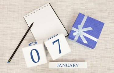 Calendar with trendy blue text and numbers for January 7 and a gift in a box.