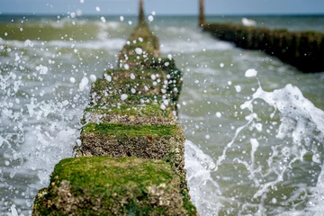 Gordijnen Close up beach poles splashed by water at the sea coast © fotografiecor
