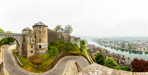 Citadel of Namur fortress walls with curved road and Meuse river  with city panorama, Namur, Wallonia, Belgium - obrazy, fototapety, plakaty