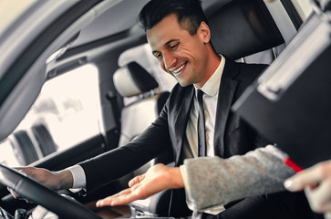 Successful young businessman in a suit chooses a new car. The seller helps to choose a car.