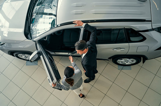 Top View Of Professional Salesperson During Work With Customer At Car Dealership. Successful Young Businessman In A Suit Chooses A New Car.