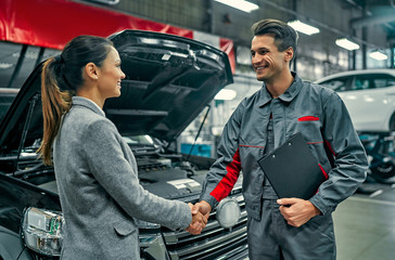 Fototapeta Beautiful businesswoman and auto service mechanic shaking hands. Car repair and maintenance. obraz