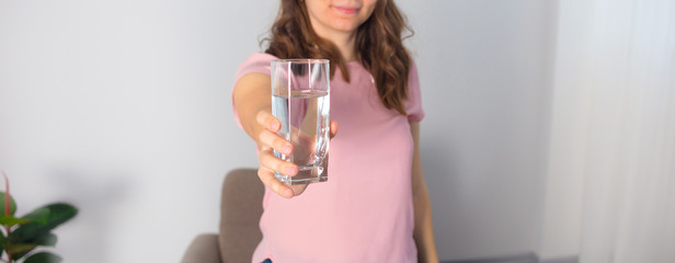A young woman holds a glass of water on a light background.