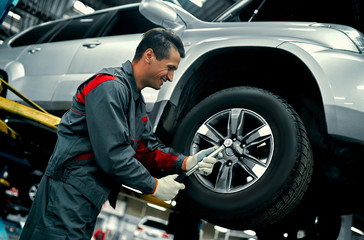 Handsome mechanic in uniform is working in auto service. Car repair and maintenance. Holding car...