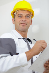 male builder or manual worker in helmet writing on clipboard