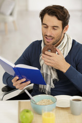 man in wheelchair reading book and eating chocolate donut