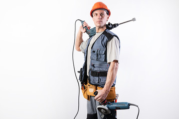 A builder with a hammer drill on his shoulder, and a angle grinder in his other hand, in a helmet,...