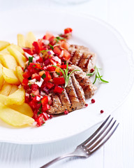 Fried pork tenderloin with tomato salsa and french fries. Bright background.