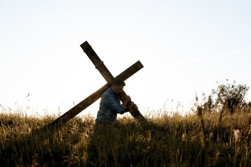 Male carrying a hand made a wooden cross through the dry grassy field