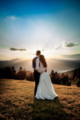 Bride and groom watch the sunset standing on the hill