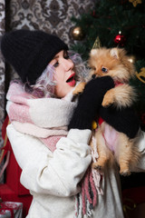 Obraz premium Beautiful happy woman plays with a little dog on the background of a Christmas tree
