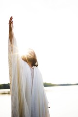 Vertical shot of Jesus Christ with his hand up towards the sky while the sun shines near his head