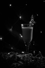 black and white photo new year's glass with drink, cocktail decorated in new year's style, branch, clothespin and berry, on a dark background