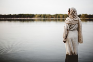 Shallow focus shot from behind of a female wearing a biblical gown while standing in the water