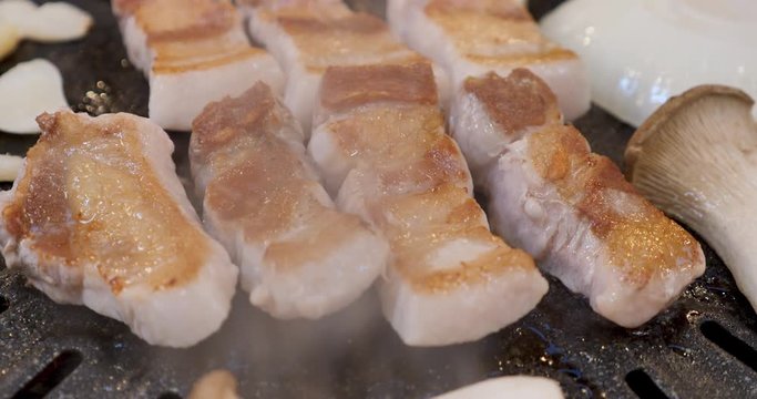 Closeup of chunks of pork belly, mushrooms and garlic sizzling on a Korean barbecue.
