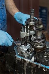Naprawa mechanicznej skrzyni biegów samochodu przez mechanika. Rozkręcanie kluczem nasadowym uszkodzonej skrzyni biegów. 