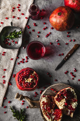 Red pomegranate juice in a glass, ripe and cut pomegranate and a sprig of mint on a gray background.