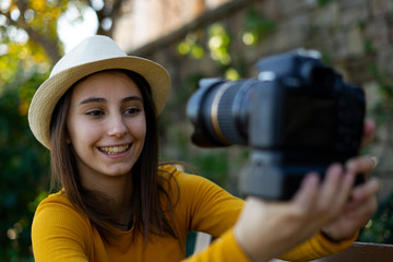 Woman vlogger and influencer with hat recording a video with a reflex camera for her blog.