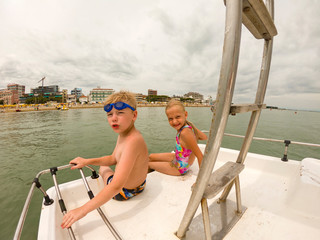 boy and girl sit near children's slide on pedal catamaran next to his father and brother. Dad, son...