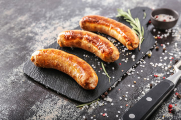 Slate plate with tasty grilled sausages with spices on dark background