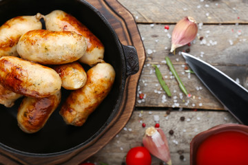 Frying pan with tasty grilled sausages on wooden table