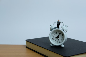 Miniature business concept - a man standing above clock and notebook. workload concept