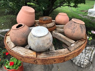 Composition of old cracked clay pots on an old rusty cart wheel on the background of nature. Mobile photo in natural daylight.