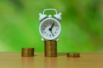 time is money concept - pile of money with white clock on a wooden table