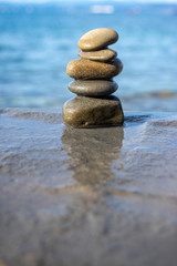 Fototapeta na wymiar Five stones cairn tower, rock zen sculpture, brown beige pebbles and sea light blue background