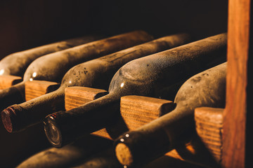 Wooden holder with bottles of wine in dark cellar, closeup