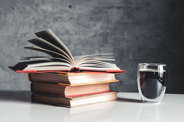 A cup of coffee near of stack of books on grey background