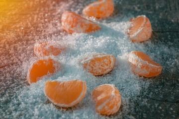 pieces of tangerine in the snow in winter on a wooden background