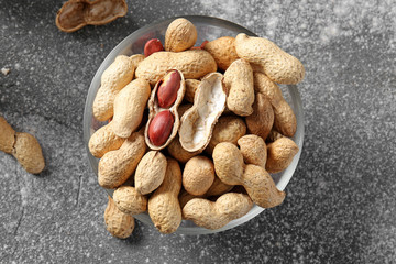 Bowl with peanuts on grey background