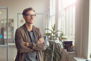 Waist up portrait of handsome adult businessman standing with arms crossed in office and looking to...