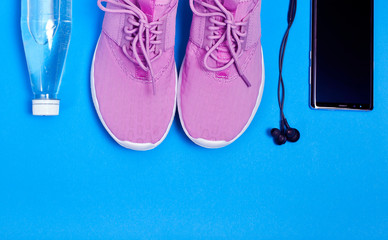 Pink sport shoes, smartphone with earphones and bottle of water on a blue background. Concept healthy lifestyle, sport and diet. 