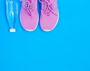 Pink sport shoes and bottle of water on a blue background. Concept healthy lifestyle, sport and diet. Text space. Top view. Flat lay. 