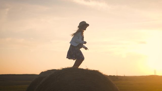 Little girl in a field with hay jump at sunset. Girl near a hay bale in the countryside.