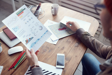 High angle view at unrecognizable modern businessman holding statistics report with colored data while working at wooden desk in office, copy space
