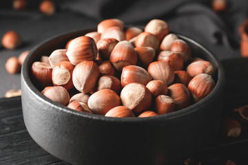 Bowl with tasty hazelnuts on dark background