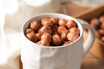 Mug with tasty hazelnuts on table, closeup