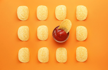 Tasty potato chips and tomato sauce on color background