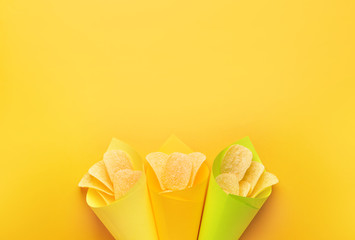 Paper cones with tasty potato chips on color background