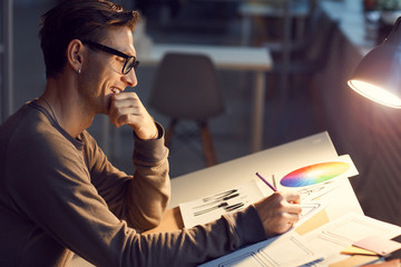 Side view portrait of contemporary male designer drawing sketches at desk while working in studio...
