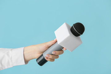 Journalist's hand with microphone on color background