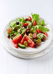 Healthy Salad with Cucumber, various Tomatoes and Olives on bright wooden Background. Healthy Snack Idea. 