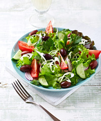 Healthy Salad with Tomatoes, Cucumber,  Lettuce and Olives on bright wooden Background. Healthy Snack Idea. 