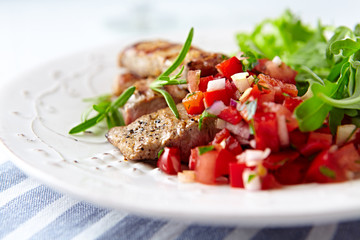 Fried pork tenderloin with tomato salsa. Bright background. Close up. 