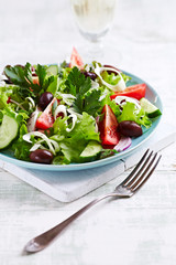 Healthy Salad with Tomatoes, Cucumber,  Lettuce and Olives on bright wooden Background. Healthy Snack Idea. 