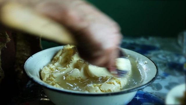 Strain out butter from whey. old woman's hand with a wooden spoon prepares butter.
